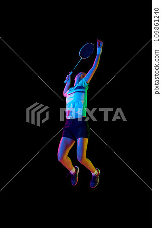Professional female badminton player training in motion against black background in neon light. 109861240