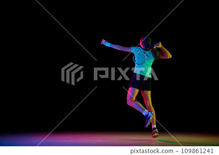 Energetic rear view portrait of featuring skilled badminton player showcasing her moves against black background in neon light. 109861241