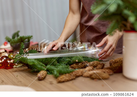 Woman making Christmas arrangement with fir branches and pine cones. craft handmade decor. 109861624