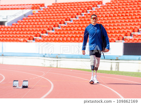 Sport man athlete prosthesis legs with sun glasses carry the bag and walk on the track of the stadium with day light. Sport man athlete prosthesis legs with sun glasses carry the bag and walk on the track of the stadium with day light. 109862169
