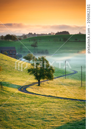 Rural scene with curved road, tree and small village in the valley and foggy morning at Switzerland 109862281