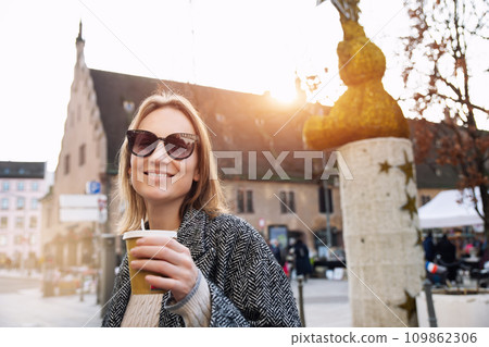Portrait young beautiful happy smiling woman drinking coffee to go tea in eco sustainable paper cup wear wool coat enjoy walking european Strasbourg city street. Stylish female person urban lifestyle Portrait young beautiful happy smiling woman drinking coffee to go tea in eco sustainable paper cup wear wool coat enjoy walking european Strasbourg city street. Stylish female person urban lifestyle 109862306