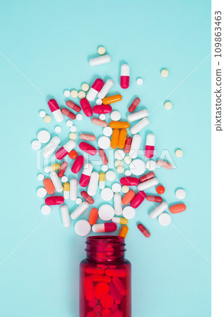 Orange bottle container with various colorful medication tablets and capsules on blue background. Concept of healthcare and medicine. Top view 109863463