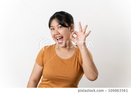 The cheerful young Asian woman smiling and showing the OK hand sign standing on white background. The cheerful young Asian woman smiling and showing the OK hand sign standing on white background. 109863561