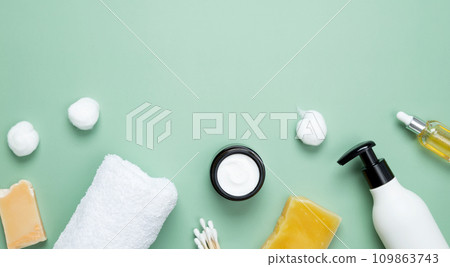 Different cosmetic bottles and container. Bathing products in the bathroom, spa serum, natural soap, cotton towel and various accessories flat lay on green background. Top view, copy space 109863743