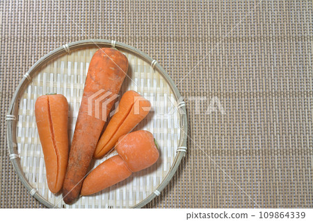 Four damaged substandard carrots placed on a bamboo colander, aligned to the left 109864339