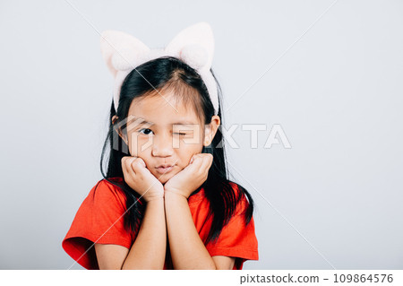 An adorable Asian girl child laughs with delight showcasing a broad smile and cheerful eyes. Isolated portrait of a happy open-mouthed kid in a red t-shirt on a white background. 109864576