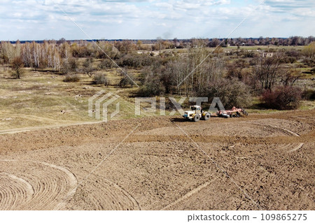 Agricultural machinery in a field near a small grove, aerial view. Agricultural land. Agricultural machinery in a field near a small grove, aerial view. Agricultural land. 109865275