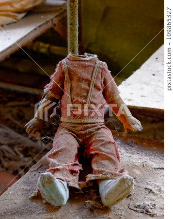 A doll with stretched arms and tattered clothes in an abandoned building. Childrens doll without a head. A dirty, broken children's toy from a radiation-contaminated kindergarten in Chernobyl. A doll with stretched arms and tattered clothes in an abandoned building. Childrens doll without a head. A dirty, broken children's toy from a radiation-contaminated kindergarten in Chernobyl. 109865327