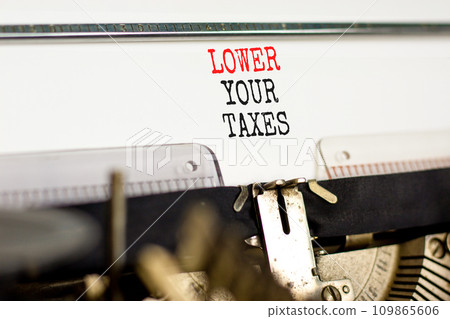 Lower your taxes symbol. Concept words Lower your taxes typed on an old retro typewriter on a beautiful white paper background. Business tax lower your taxes concept. Copy space. 109865606