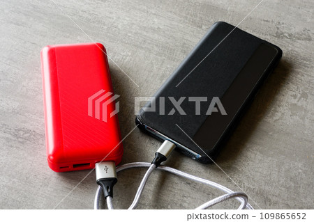 Modern black smart phone charging with help of red power bank, powerbank charges the phone 109865652