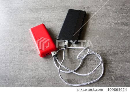 Modern black smart phone charging with help of red power bank, powerbank charges the phone 109865654