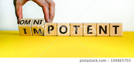 Hand is turning cubes and changes the word 'impotent' to 'omnipotent' or vice versa. Beautiful yellow table, white background. Medical concept. Copy space. Hand is turning cubes and changes the word 'impotent' to 'omnipotent' or vice versa. Beautiful yellow table, white background. Medical concept. Copy space. 109865703