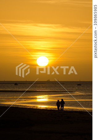 Couple strolling along the beach at sunset. 109865985