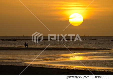 Couple strolling along the beach at sunset. Couple strolling along the beach at sunset. 109865988