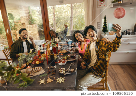 Happy people taking selfie photo sitting on holiday dinner party at home and looks camera with smile Happy people taking selfie photo sitting on holiday dinner party at home and looks camera with smile 109866130