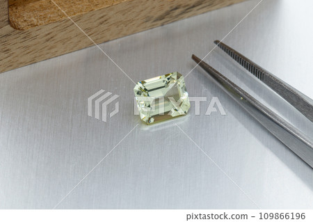 macro mineral faceted stone heliodor, Golden beryl with tweezers on a gray background 109866196