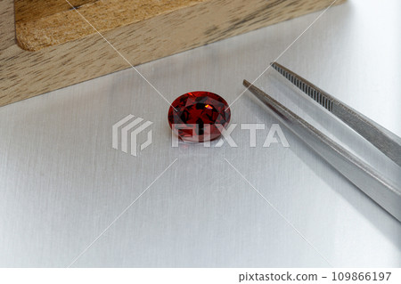 macro mineral faceted stone Garnet with tweezers on a gray background 109866197