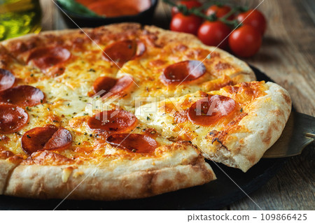 A slice of hot Italian pizza with stretching cheese. Pizza pepperoni on a dark wooden background 109866425
