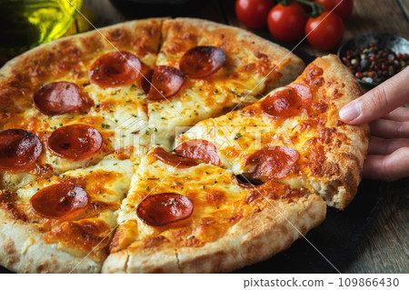 A slice of hot Italian pizza with stretching cheese. Pizza pepperoni on a dark wooden background A slice of hot Italian pizza with stretching cheese. Pizza pepperoni on a dark wooden background 109866430