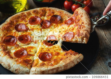 A slice of hot Italian pizza with stretching cheese. Pizza pepperoni on a dark wooden background A slice of hot Italian pizza with stretching cheese. Pizza pepperoni on a dark wooden background 109866431
