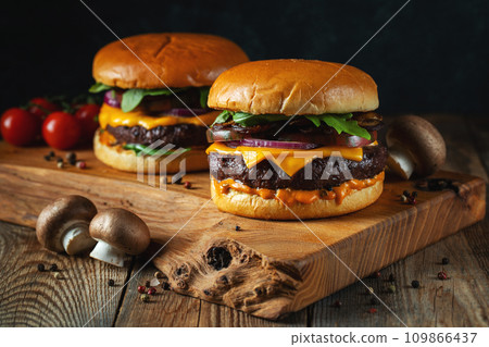 Two delicious homemade burgers of beef, cheese and mushrooms on an wooden table. Fat unhealthy food Two delicious homemade burgers of beef, cheese and mushrooms on an wooden table. Fat unhealthy food 109866437
