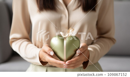 a woman holds a heart shaped gift box with a green ribbon 109867152