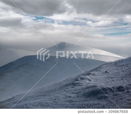 Snow covered mountain slope in last evening sunlight. Magnificent windy dusk on tops above picturesque alpine ski resort, Dragobrat, Ukraine, Carpathian Mountains. Snow covered mountain slope in last evening sunlight. Magnificent windy dusk on tops above picturesque alpine ski resort, Dragobrat, Ukraine, Carpathian Mountains. 109867688