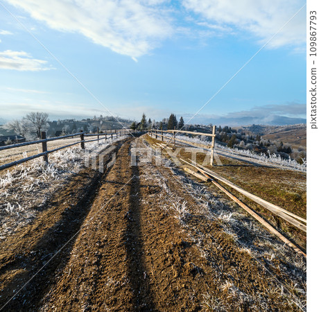 Winter coming. Last days of autumn, morning in mountain countryside peaceful picturesque hoarfrosted scene. Dirty road from hills to the village. Ukraine, Carpathian mountains. 109867793