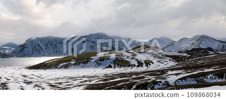 Season change in the Icelandic highlands. Colorful Landmannalaugar mountains under snow cover in autumn. Frostastadavatn lake at the foot of the mountains. Season change in the Icelandic highlands. Colorful Landmannalaugar mountains under snow cover in autumn. Frostastadavatn lake at the foot of the mountains. 109868034