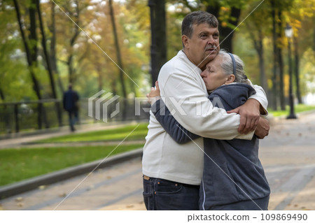An elderly couple hugs in the park during the walk. 109869490