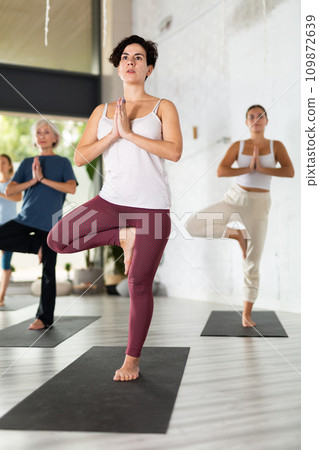 Young Latin woman balancing in Tree position on mat during group yoga class 109872639