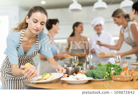 Girl visitors to culinary school decorates finished dish, fried chicken fillet with golden crust. 109872642