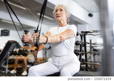 Active athlete mature woman during exercises on crossover exercise machine with loops and weighting Active athlete mature woman during exercises on crossover exercise machine with loops and weighting 109872834