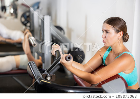 Young woman trains her arm muscles on machine Young woman trains her arm muscles on machine 109873068