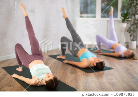 Diligent women practicing bridge pose of yoga in light fitness room 109873925