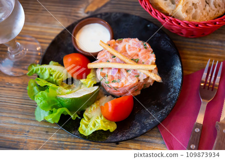 Salmon tartare with chive cream, vegetables, lime and breadsticks 109873934