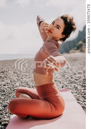 Middle aged well looking woman with black hair, fitness instructor in leggings and tops doing stretching and pilates on yoga mat near the sea. Female fitness yoga routine concept. Healthy lifestyle 109875478