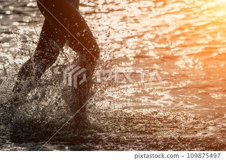 Running woman on a summer beach. A woman jogging on the beach at sunrise, with the soft light of the morning sun illuminating the sand and sea, evoking a sense of renewal, energy and health. Running woman on a summer beach. A woman jogging on the beach at sunrise, with the soft light of the morning sun illuminating the sand and sea, evoking a sense of renewal, energy and health. 109875497