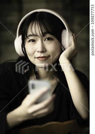 一位女士在別緻的房間裡用智慧型手機聽音樂 一位女士在別緻的房間裡用智慧型手機聽音樂 109877753