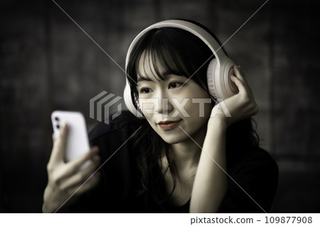 A woman listening to music on her smartphone in a chic room A woman listening to music on her smartphone in a chic room 109877908