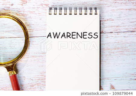 AWARENESS a word written on a notebook on wooden boards next to a magnifying glass AWARENESS a word written on a notebook on wooden boards next to a magnifying glass 109879044