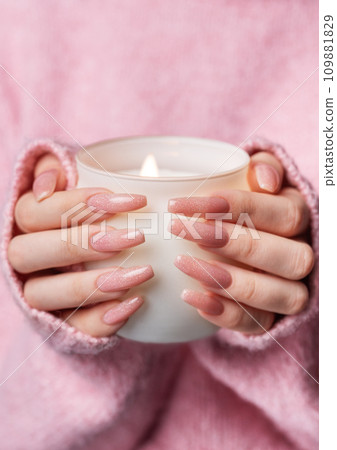Woman in a pink sweater with a pink manicure holds a candle Woman in a pink sweater with a pink manicure holds a candle 109881829