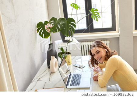 Smiling female freelancer working on laptop at home 109882362