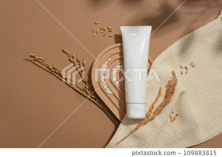 A plastic tube and rice are displayed on a domed platform next to a beige cloth on a brown background. Blank label for lettering design. Vegan cosmetics with rice bran extract. A plastic tube and rice are displayed on a domed platform next to a beige cloth on a brown background. Blank label for lettering design. Vegan cosmetics with rice bran extract. 109883815