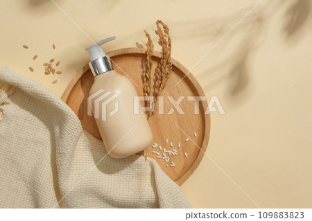 Rice and a bottle of unbranded shower gel are displayed on a round wooden tray. Beige background with leaf shadow. Exquisite space for cosmetic advertising. Rice and a bottle of unbranded shower gel are displayed on a round wooden tray. Beige background with leaf shadow. Exquisite space for cosmetic advertising. 109883823