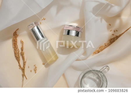 Unlabeled high-end cosmetics set showcased on a white fabric backdrop with rice. The sophisticated setting provides an ideal space for cosmetic ads. 109883826