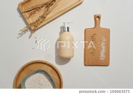 Rice bran powder is stored in a ceramic bowl. Wooden trays with different shapes and a bottle of shower gel on a white background. Natural extracts in cosmetics. Rice bran powder is stored in a ceramic bowl. Wooden trays with different shapes and a bottle of shower gel on a white background. Natural extracts in cosmetics. 109883875