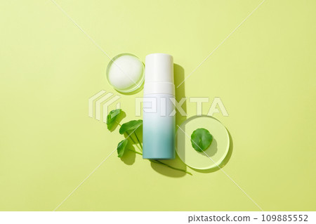 An unlabeled cosmetic bottle, glass podium and fresh pennywort leaves stand out against the background. Ideal space for advertising cosmetics with pennywort extract. 109885552