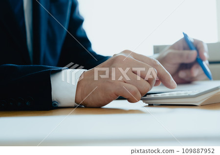 Hand of a man in a suit calculating with a calculator Hand of a man in a suit calculating with a calculator 109887952